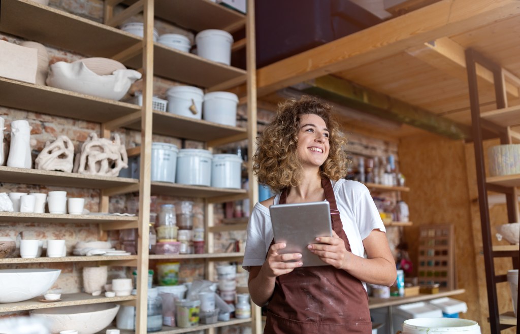 A craftswoman holding a tablet computer in her art studio